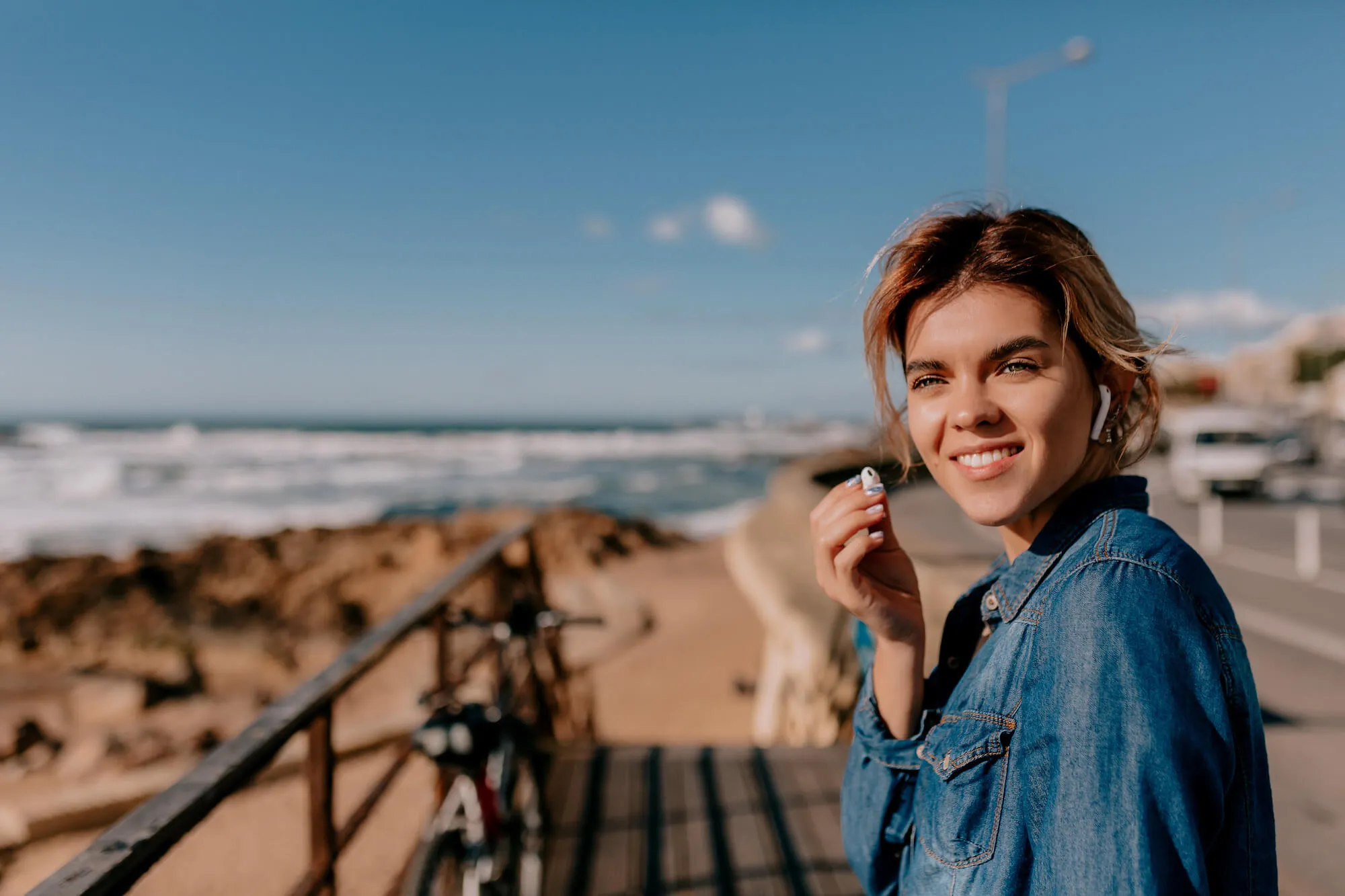 Woman at the seaside with earbuds in her ears.